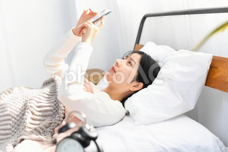 ベッドでスマホを見る笑顔のアジア人女性 ベッド,スマートフォン,女性の写真素材