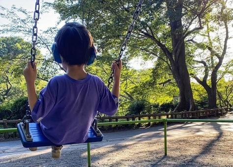 イヤマフをつけてブランコに乗る子ども イヤマフをつけてブランコに乗る子どもの写真