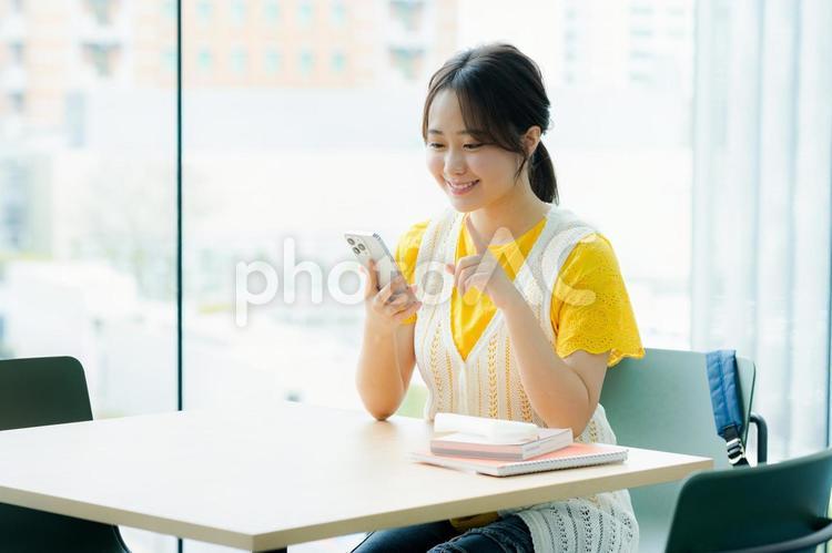 カフェでスマホを見る学生 スマホ,若い女性,笑顔の写真素材