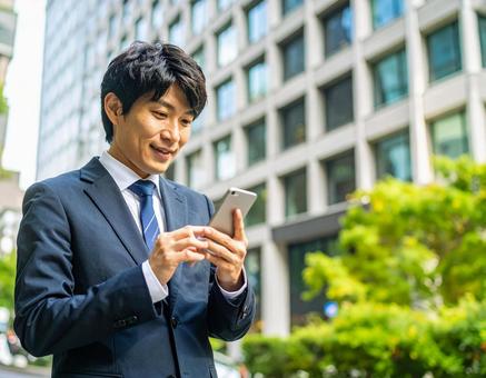 オフィス街でスマホを操作する男性社員の写真