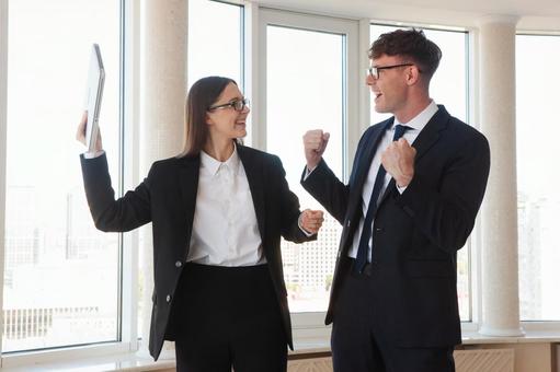 ガッツポーズで喜ぶ窓際の男女 男女,ガッツポーズ,笑顔の写真素材