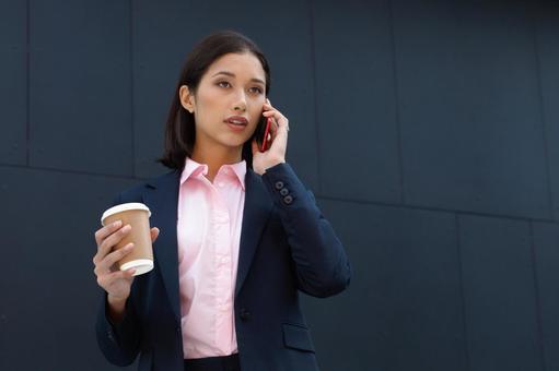 オフィスビルの外でコーヒー片手に電話している女性 ビジネスウーマン,ビジネス,女性の写真素材