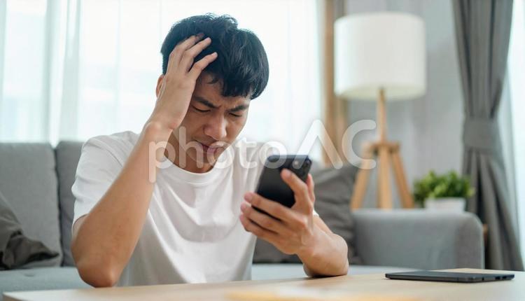 自宅でスマホを見て困惑する若い男性 人物,男性,10代の写真素材