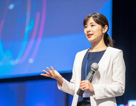 ステージ上でプレゼンをする女性の写真