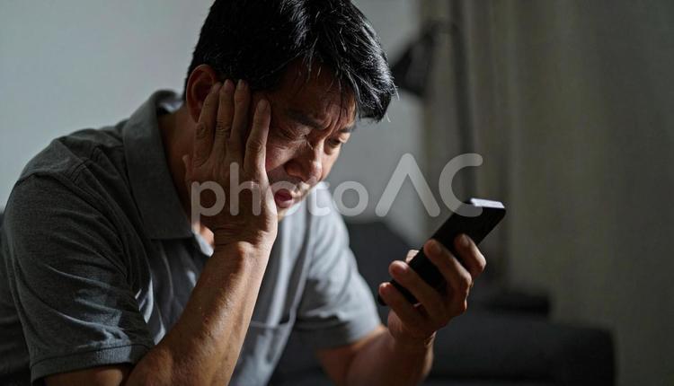暗い部屋でスマほを見つめ悩むアジア人男性 人物,男性,50代の写真素材