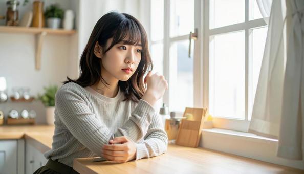 疲れた表情でキッチンに座る若い女性の写真