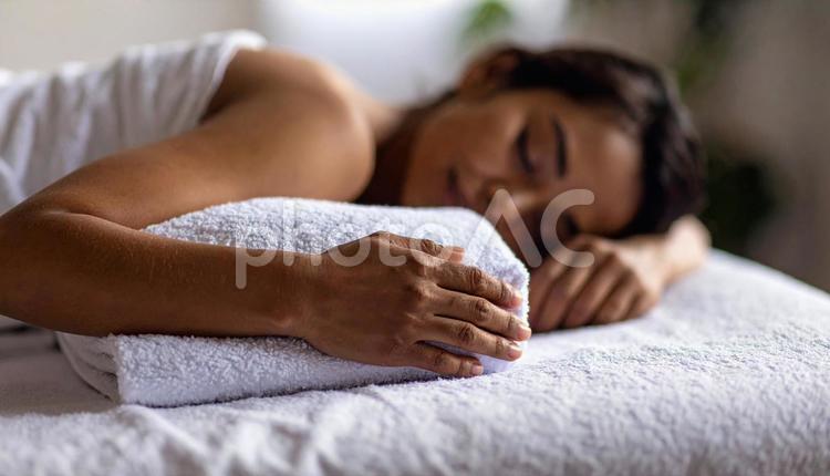 片腕の下にバスタオルを置いて眠る女性患者 バスタオル枕,首こり,背中の写真素材
