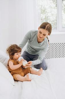 1人でミルクを飲んでいる子供をサポートする母 1人でミルクを飲んでいる子供をサポートする母 親子,哺乳瓶,飲むの写真素材