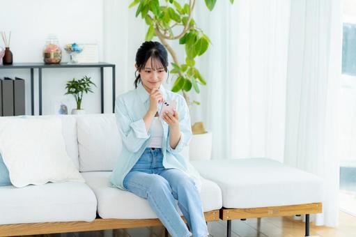 部屋でスマホを操作する若い女性 スマホ,笑顔,女性の写真素材