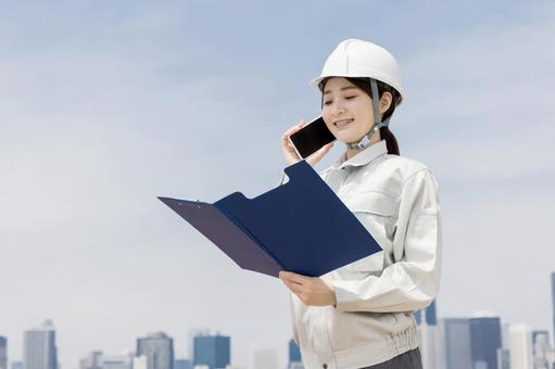 スマートフォンを使う作業服を着た若い女性 スマートフォンを使う作業服を着た若い女性 女性,人物,スマートフォンの写真素材
