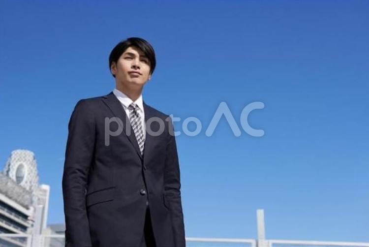 オフィス街に立つ日本人男性ビジネスマン	 ビジネスマン,青空,男性の写真素材