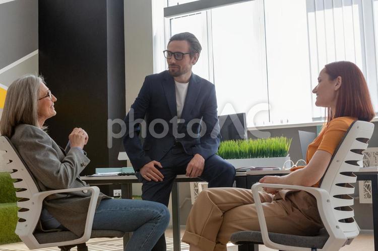 デスクで話をしている3人のビジネスパーソン ビジネスマン,ビジネスウーマン,男性の写真素材