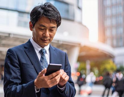 オフィス街でスマホを操作する男性社員 オフィス街でスマホを操作する男性社員の写真
