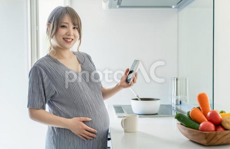 キッチンでスマートフォンを使う妊婦の女性 妊婦,スマホ,アプリの写真素材