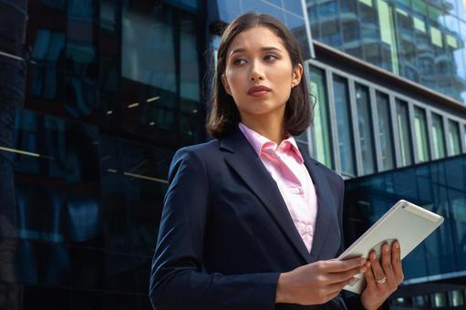 オフィスビルの外でタブレットを持って立っているスーツのアジア人ビジネスウーマン ビジネスウーマン,ビジネス,女性の写真素材