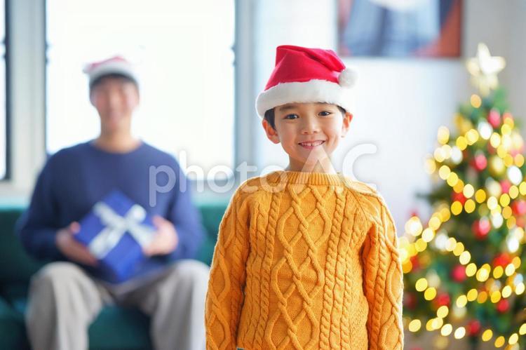 カメラ目線でサンタ帽の男の子と後ろに男性とクリスマスツリー 親子,男の子,小学生の写真素材