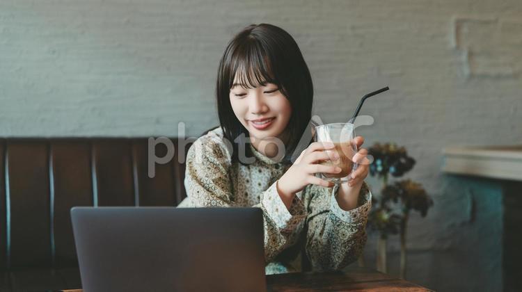 ソファに座ってパソコンを使う若い女性 女性,笑顔,パソコンの写真素材