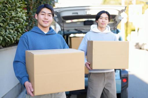 車から引っ越しの段ボール箱を運び出す2人のカメラ目線の男性 車から引っ越しの段ボール箱を運び出す2人のカメラ目線の男性 引っ越し,一人暮らし,男性の写真素材