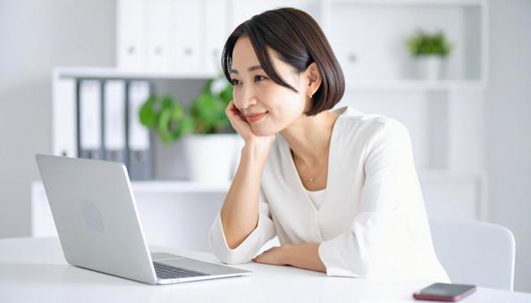 パソコンの前で考える女性社員 パソコンの前で考える女性社員の写真