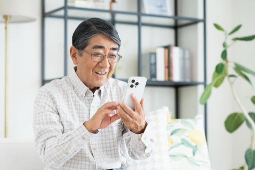 リビングでスマホを使うシニアの男性 リビングでスマホを使うシニアの男性 シニア,スマホ,男性の写真素材