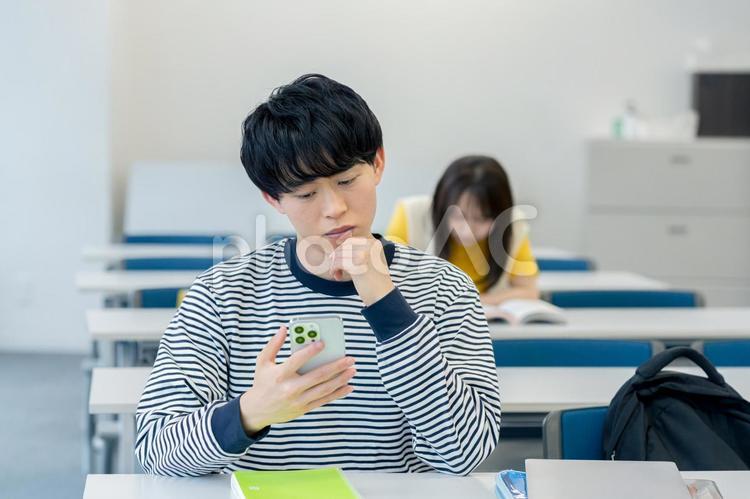 スマホを見ながら悩む大学生 スマホ,大学生,男性の写真素材