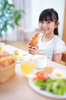 パンとジュースが並ぶ食卓で幸せそうな表情 女の子,食事,クロワッサンの写真素材