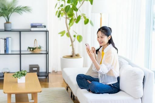 部屋でスマホを操作する女性 部屋でスマホを操作する女性 スマホ,笑顔,部屋の写真素材