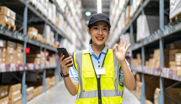 スマホを持ちOKサインの日本人女性作業員 スマホを持ちOKサインの日本人女性作業員の写真