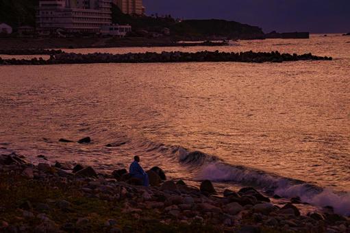 夕日に染まる海岸に打寄せる波を眺める男性 海,海岸,風景の写真素材