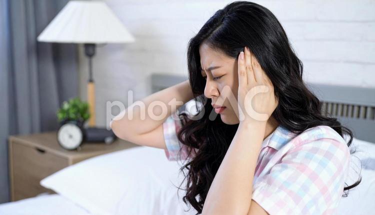 体調不良でベッドで頭を押さえる日本人女性 体調不良,低血圧,眠いの写真素材