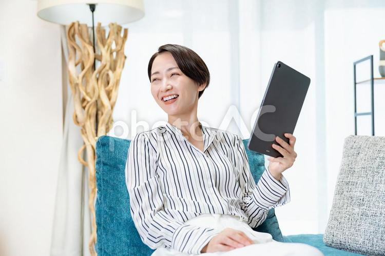 ソファに座りタブレットを見る女性 スマホ,ビジネス,メッセージの写真素材