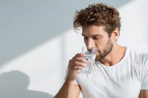 白いTシャツの男性がグラスの水を飲む 白いTシャツの男性がグラスの水を飲むの写真