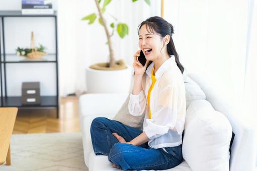 リビングでスマホで話す若い女性 リビングでスマホで話す若い女性 スマホ,笑顔,電話の写真素材