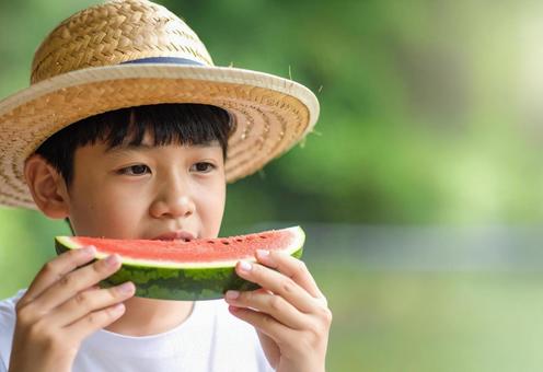 スイカにかぶりつく麦わら帽子の男の子 スイカにかぶりつく麦わら帽子の男の子の写真