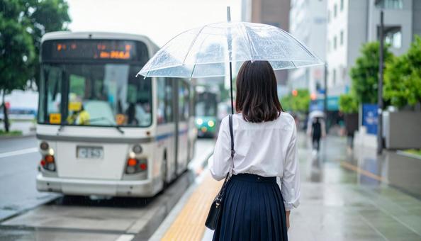 雨の中バス停でバスを待つ日本人女性の写真