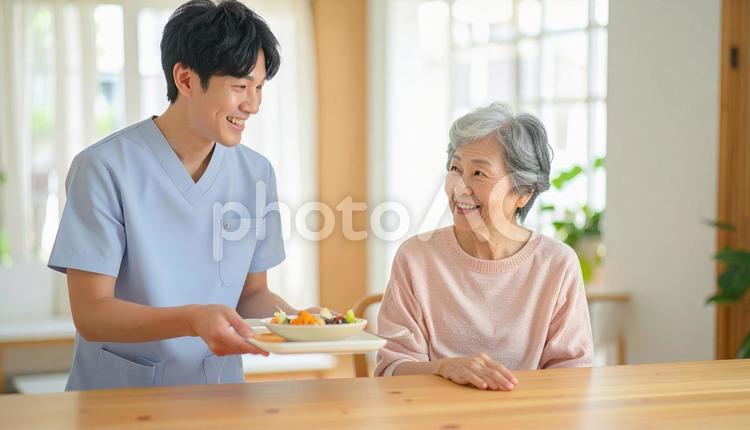 笑顔で食事を運ぶ男性介護士と高齢女性 男性介護士,訪問介護,在宅介護の写真素材