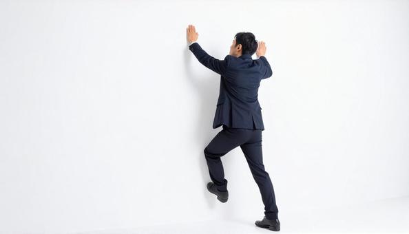 白い壁にのぼって乗り越える日本人男性 白い壁にのぼって乗り越える日本人男性の写真