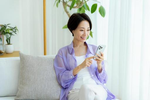 部屋でスマホを使うミドル女性 スマホ,笑顔,女性の写真素材