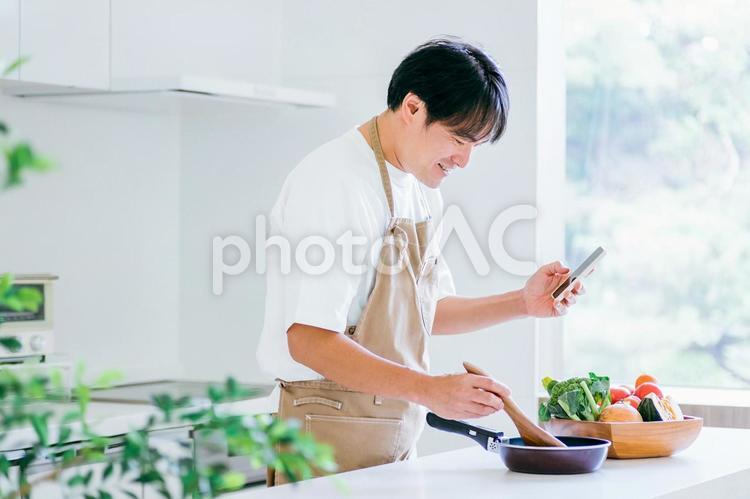 スマホを見ながら料理する男性（笑顔） 料理,レシピ,家事の写真素材