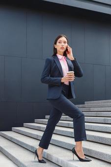 オフィスビルの外の階段でコーヒー片手に電話するアジア人ビジネスウーマン ビジネスウーマン,ビジネス,女性の写真素材