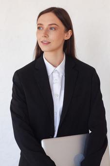 パソコンを待ち横を見る女性の写真