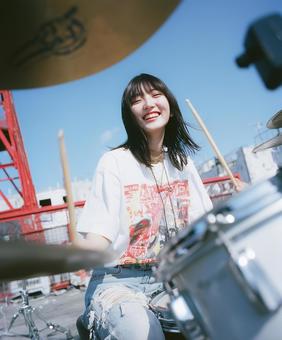 廃工場を背景にドラムを叩く笑顔の女性 廃工場を背景にドラムを叩く笑顔の女性の写真
