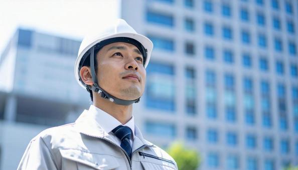 高層ビルの斜め上を見つめる若い作業服男性 高層ビルの斜め上を見つめる若い作業服男性の写真