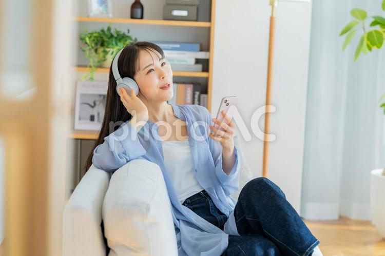 ソファでくつろぐ若い女性 スマホ,ヘッドフォン,ポートレートの写真素材