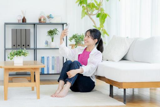 部屋でスマホを操作する若い女性 スマホ,笑顔,若い女性の写真素材