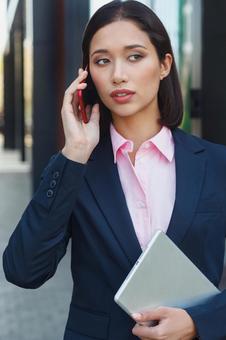 スマートフォンで電話しているビジネス街に居るビジネスウーマン ビジネスウーマン,ビジネス,女性の写真素材