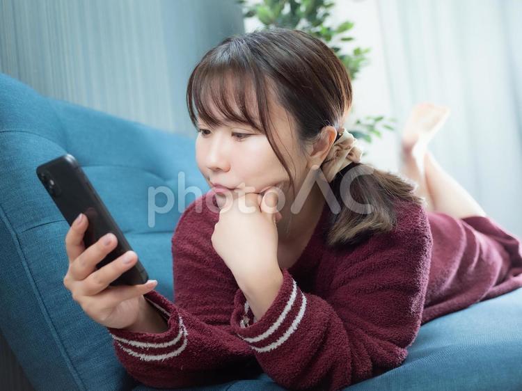 03：ソファーでスマホを操作する女性 スマホ,スマートフォン,電話の写真素材