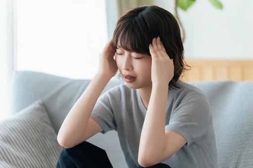 頭を押さえて悩む女性 頭を押さえて悩む女性の写真