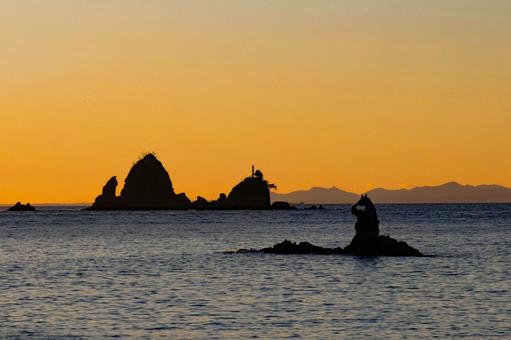 夕焼け色の空とゴジラに似た岩のシルエット 夕焼け,ゴジラ岩,シルエットの写真素材