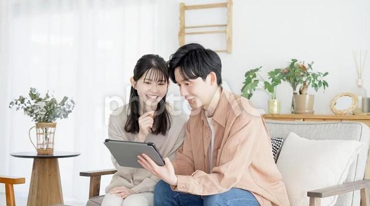 不動産サイトや旅行サイトを見るカップル 夫婦,リビング,タブレットの写真素材